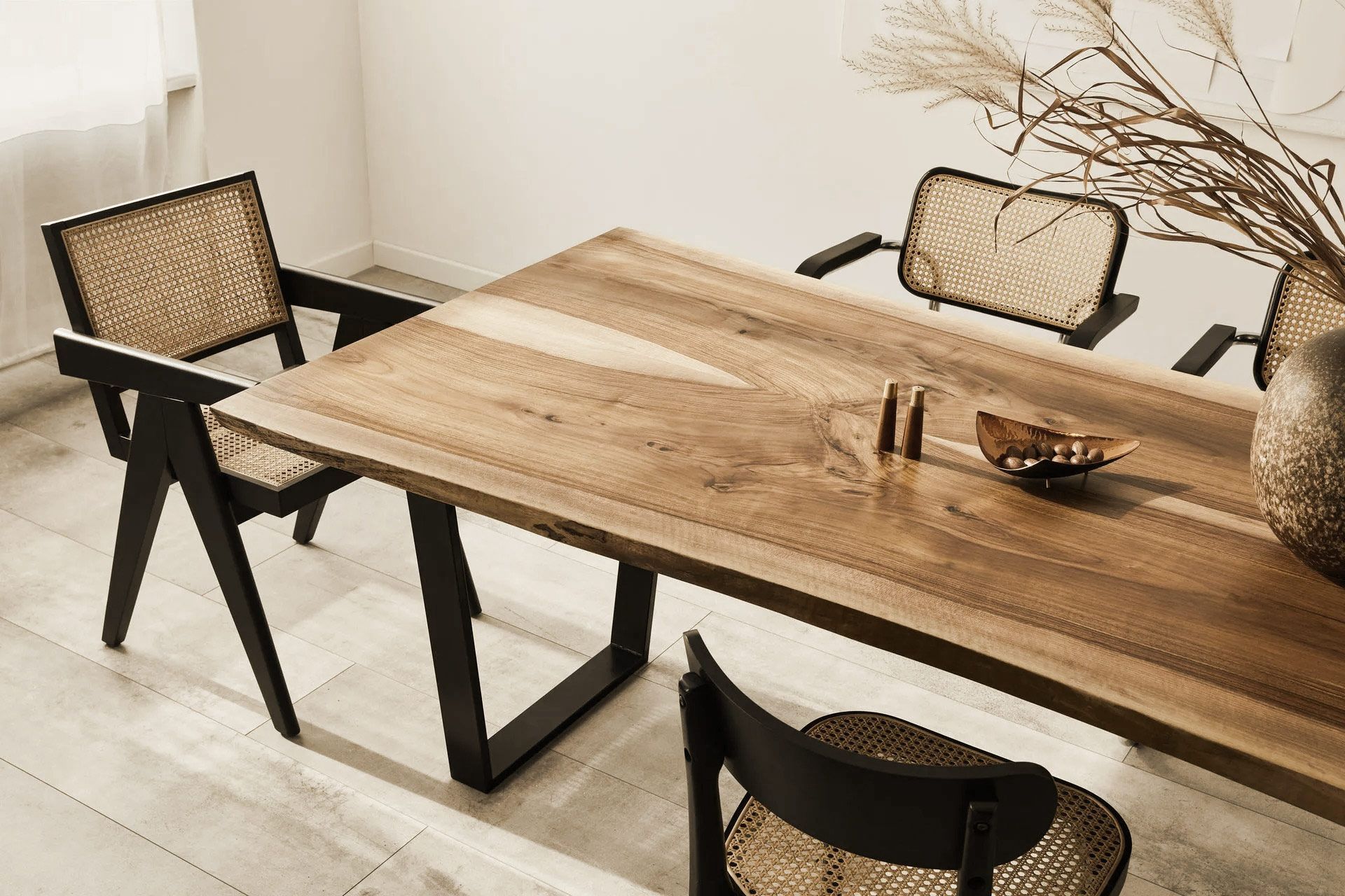 Wooden dining table with black chairs, vase of dried grasses, and a bowl on the table.