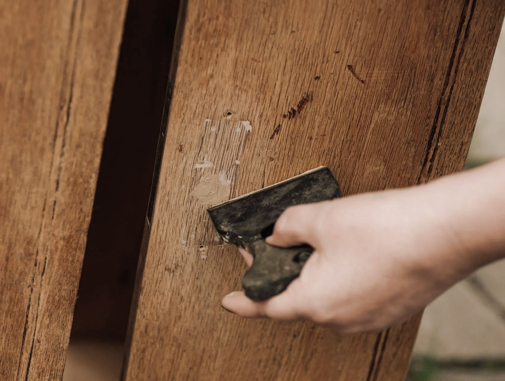 Hand scraping a small patch of damaged wood on a wooden surface.