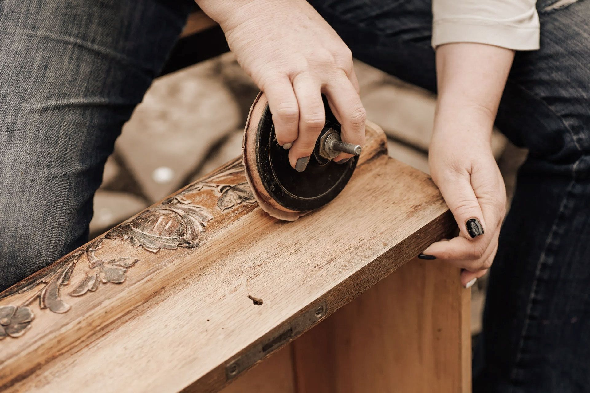 Person sanding a wooden cabinet with a circular sander.
