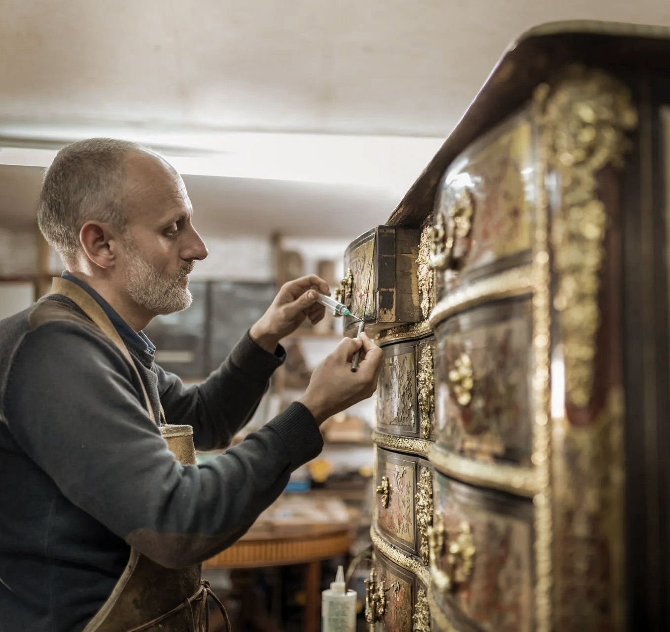 Man restoring ornate antique dresser in a workshop.
