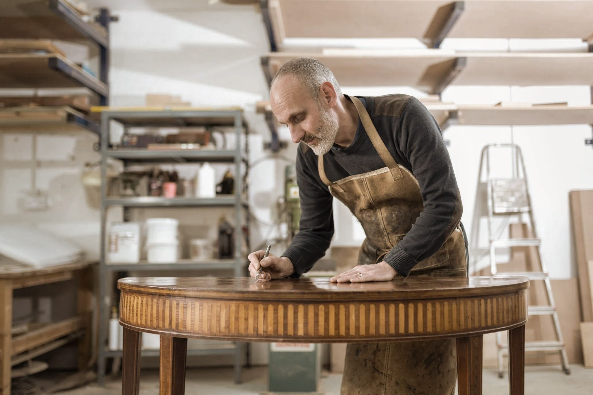 Man in apron working on a wooden table in a workshop.