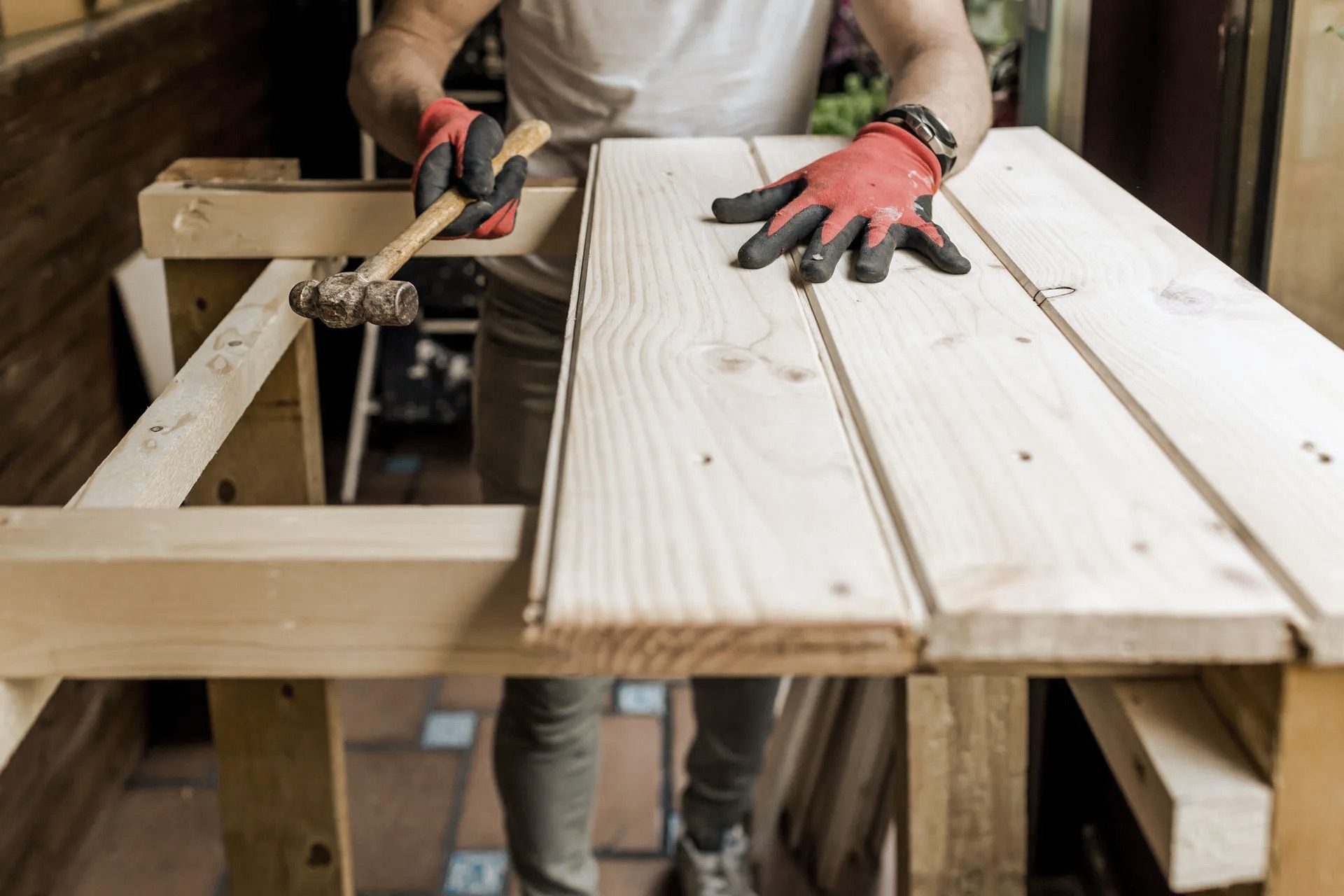 Person hammering wood planks on a wooden table, wearing work gloves.