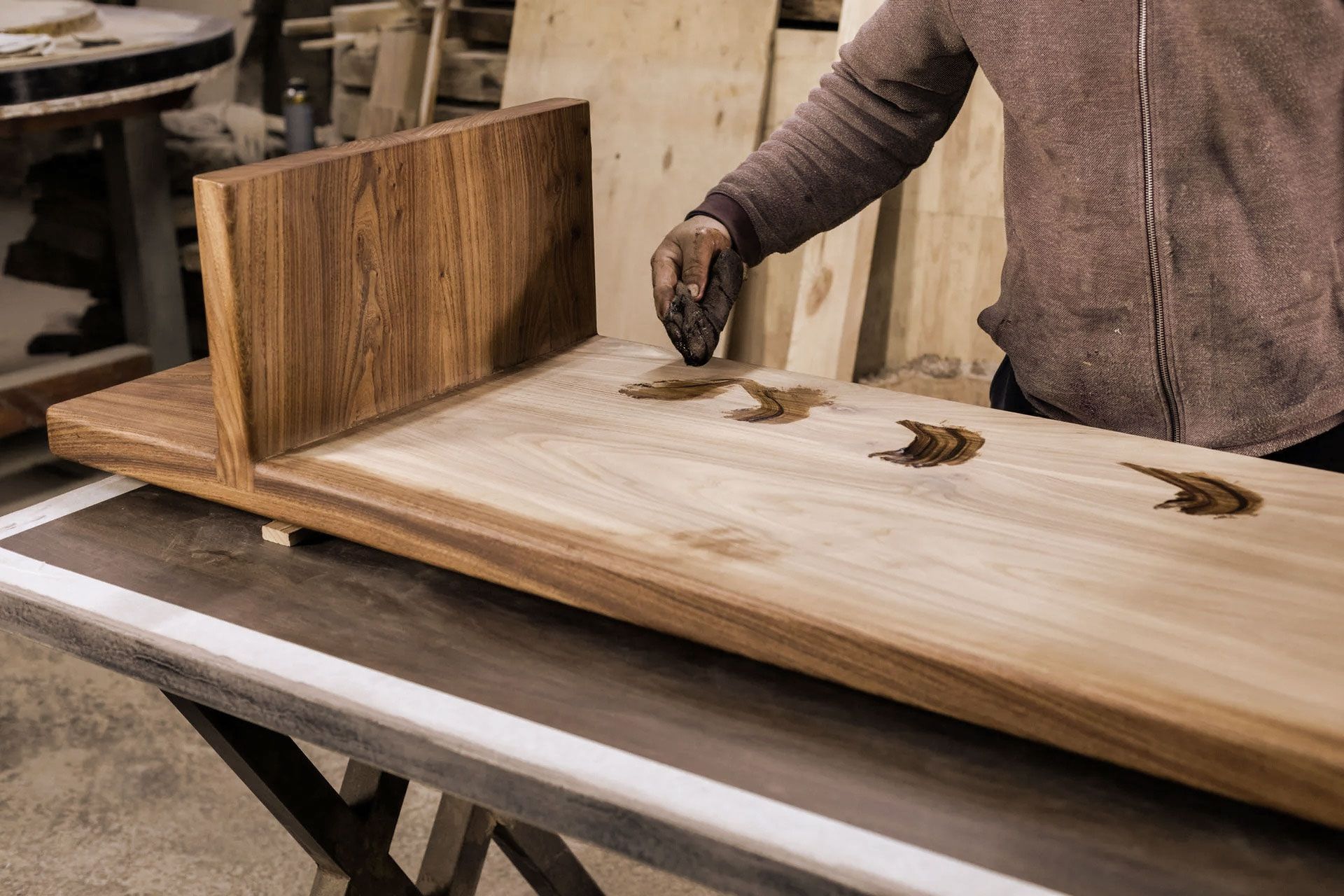 Person applying wood stain to a wooden shelf in a workshop.
