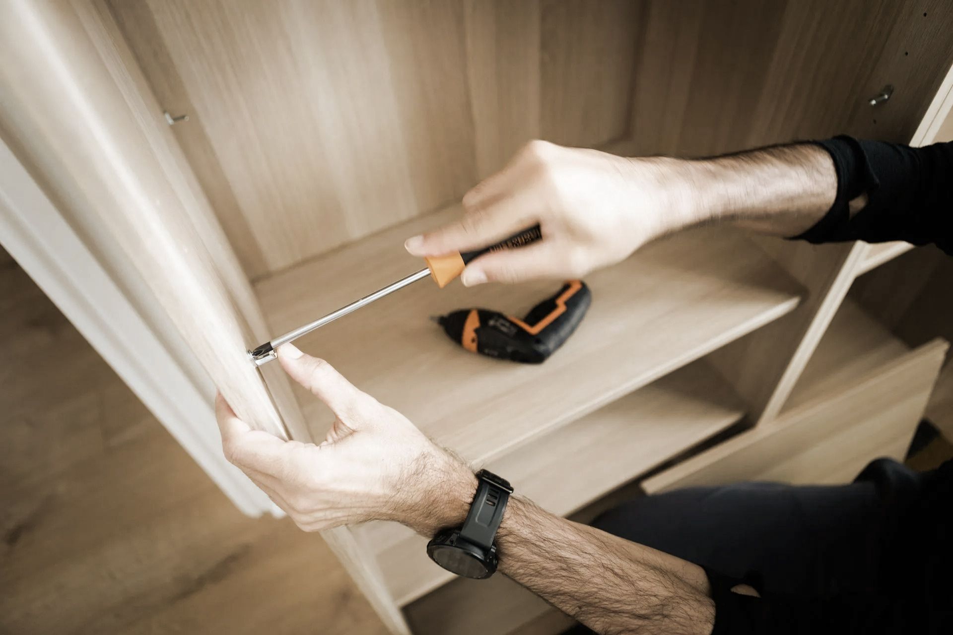 Person using a screwdriver to assemble wooden furniture inside a cabinet.