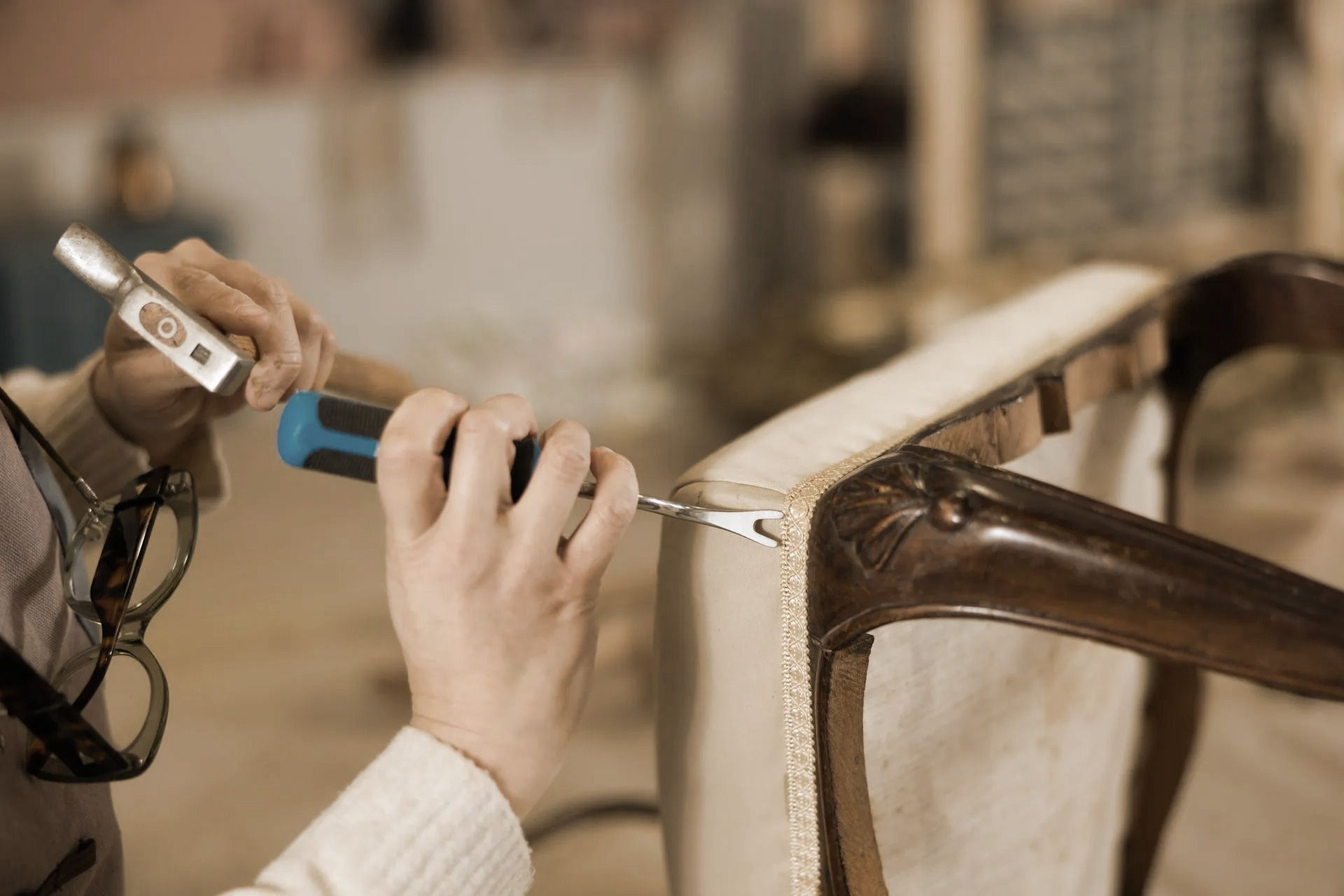 A person using a hammer and upholstery tool to work on a wooden chair frame.