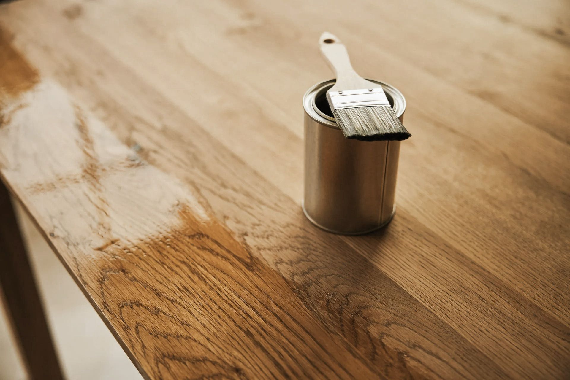 Wooden table partially coated with varnish, with a paint can and brush.