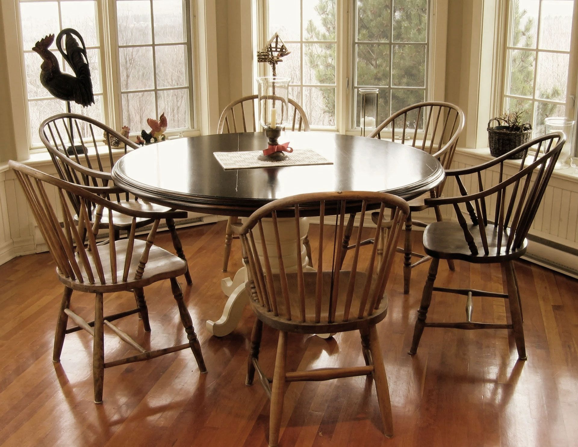 Round dining table with seven wooden chairs in a bright room with a view of outside.