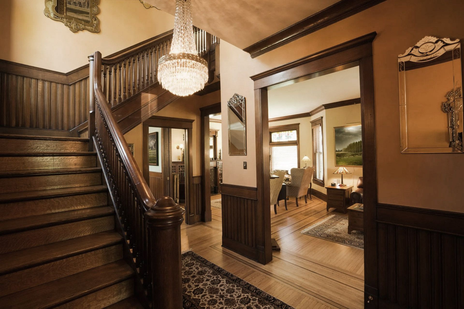 Grand foyer with a wooden staircase, chandelier, and doorway leading to a sitting area.