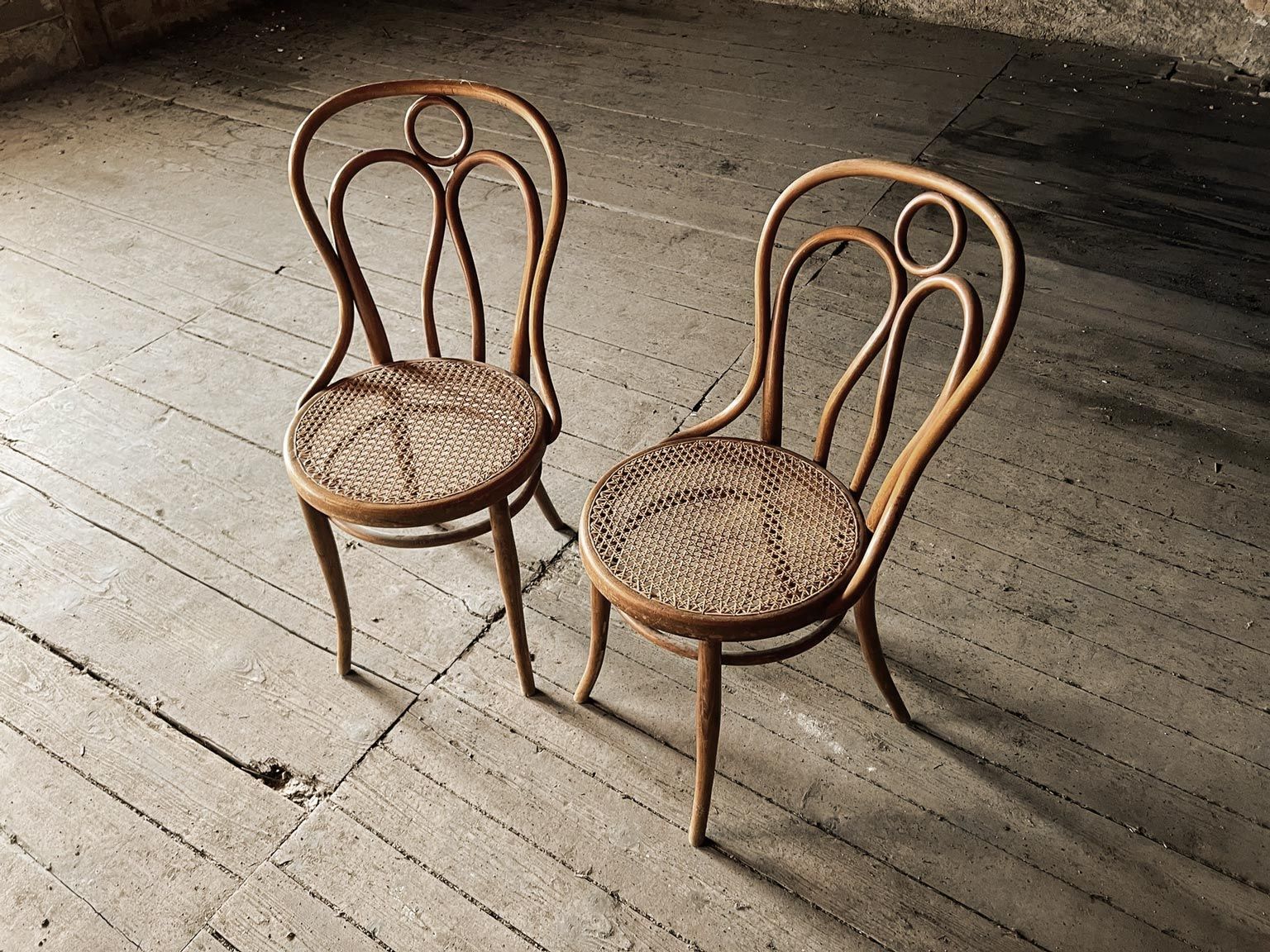 Two antique wooden chairs with woven seats, on a concrete floor.