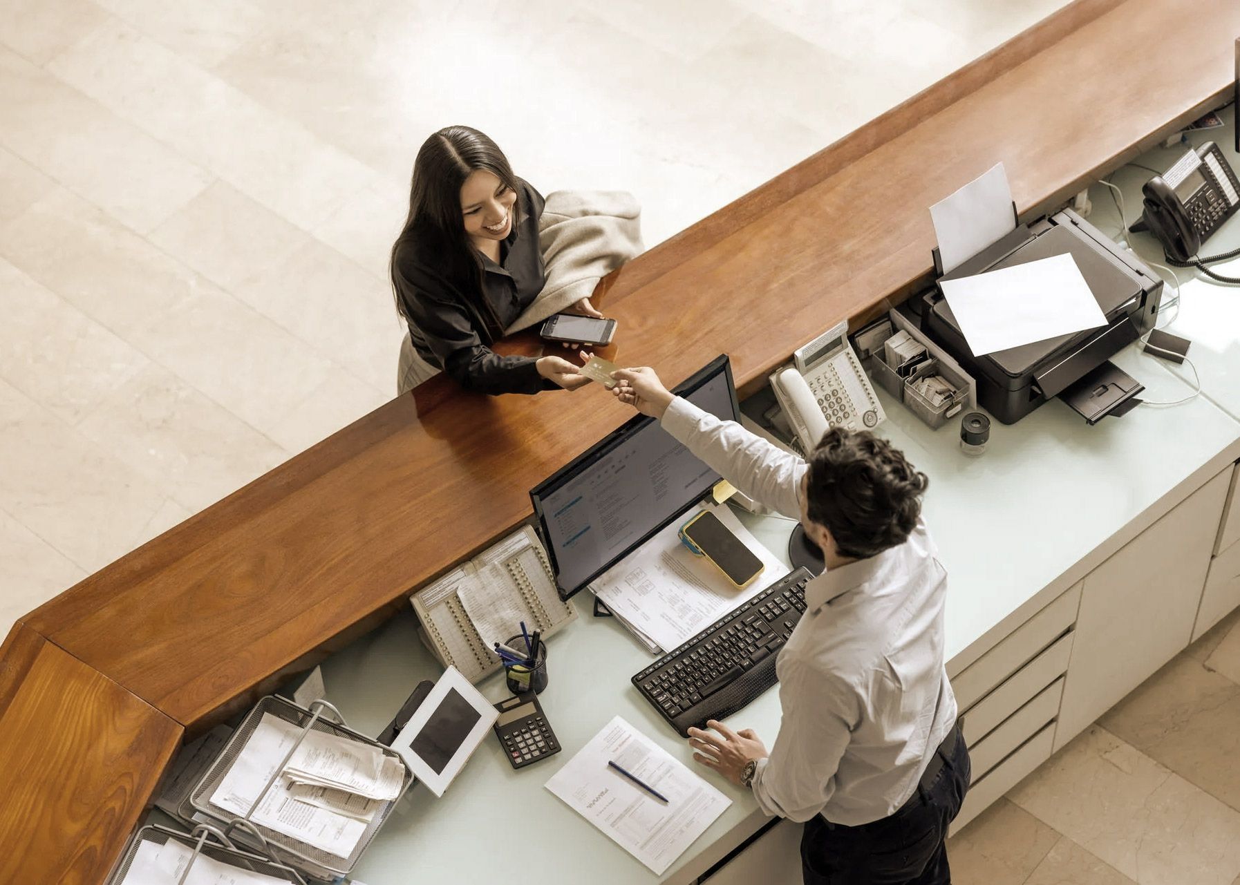 Woman at a hotel reception desk handing her credit card to the employee.