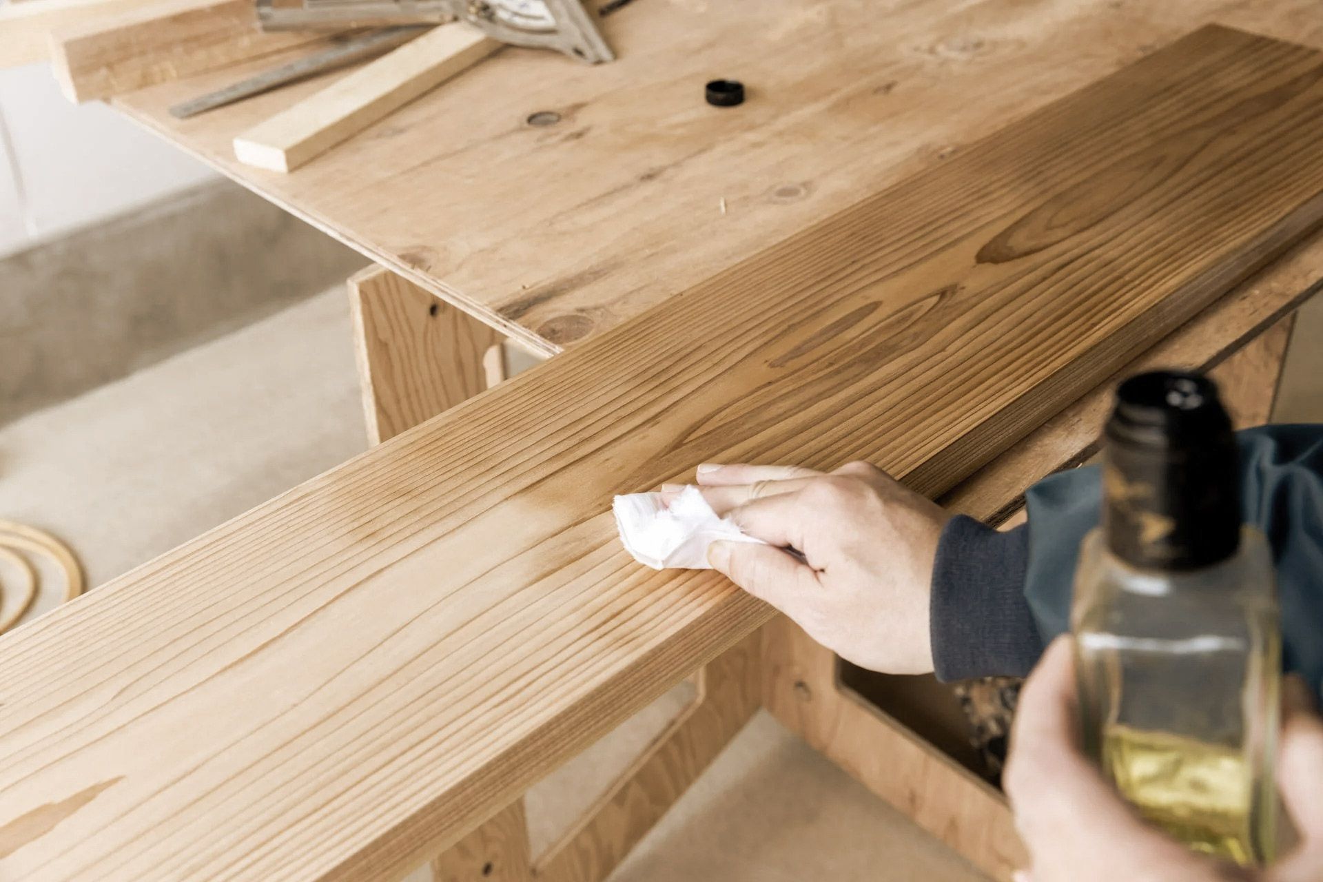 Person applying oil finish to a wooden board on a workbench with tools nearby.