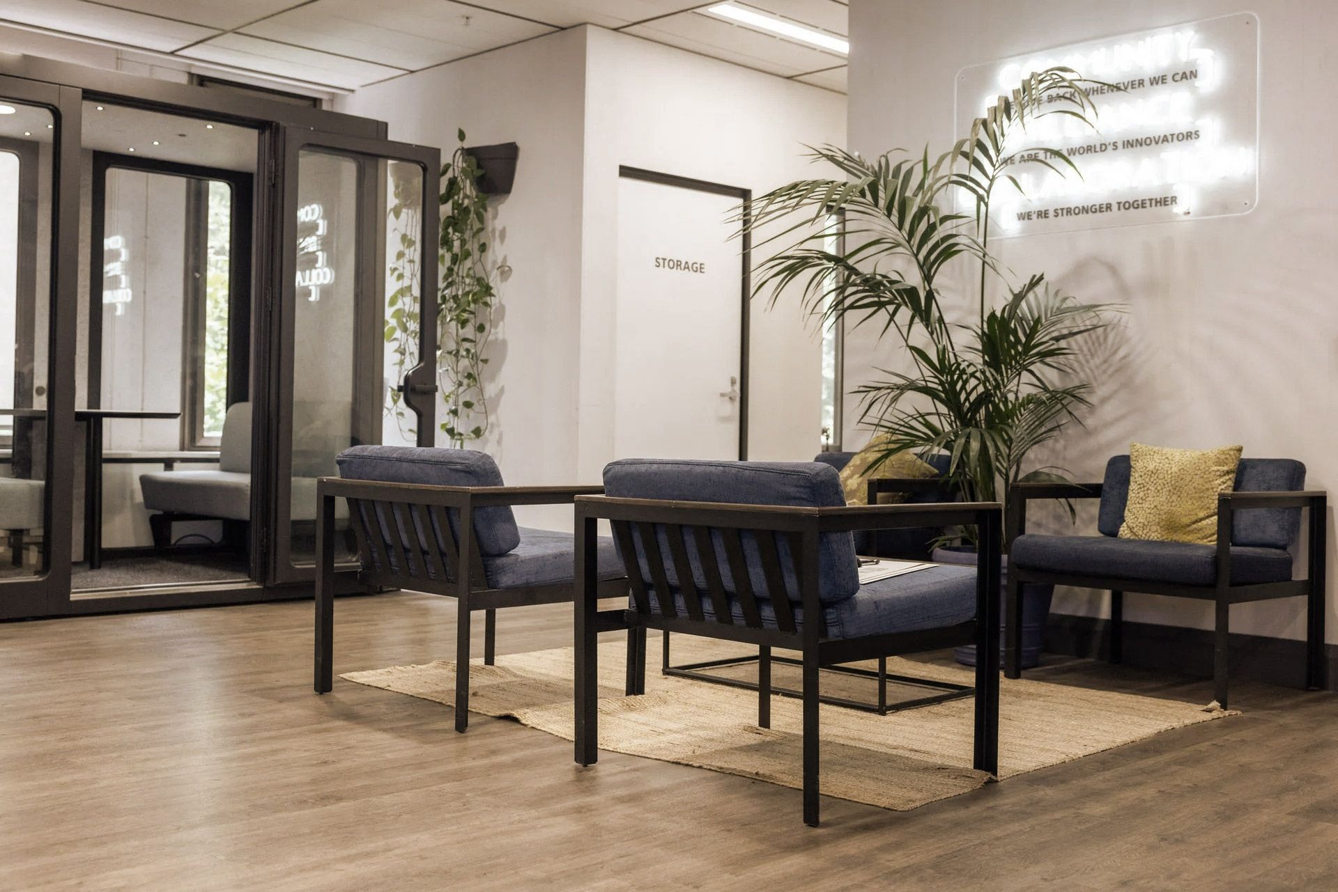 Office waiting area with blue chairs, a plant, and a neon sign.