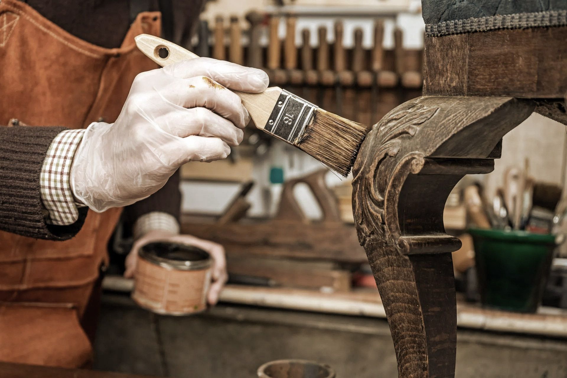 Person in gloves staining ornate wooden furniture with a brush. Workshop setting.