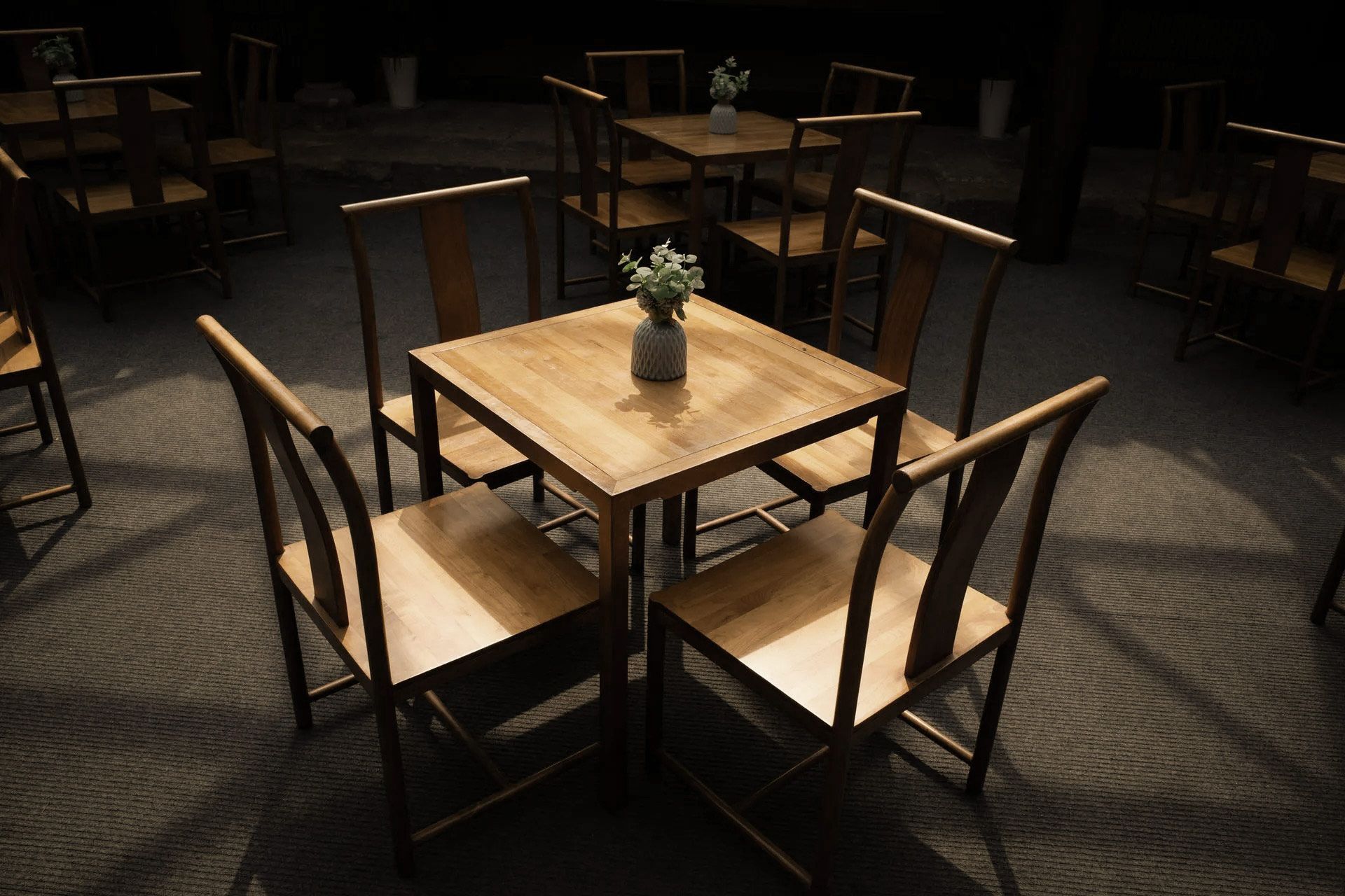 Wooden table with four chairs, a small vase of flowers. Restaurant setting with other tables.