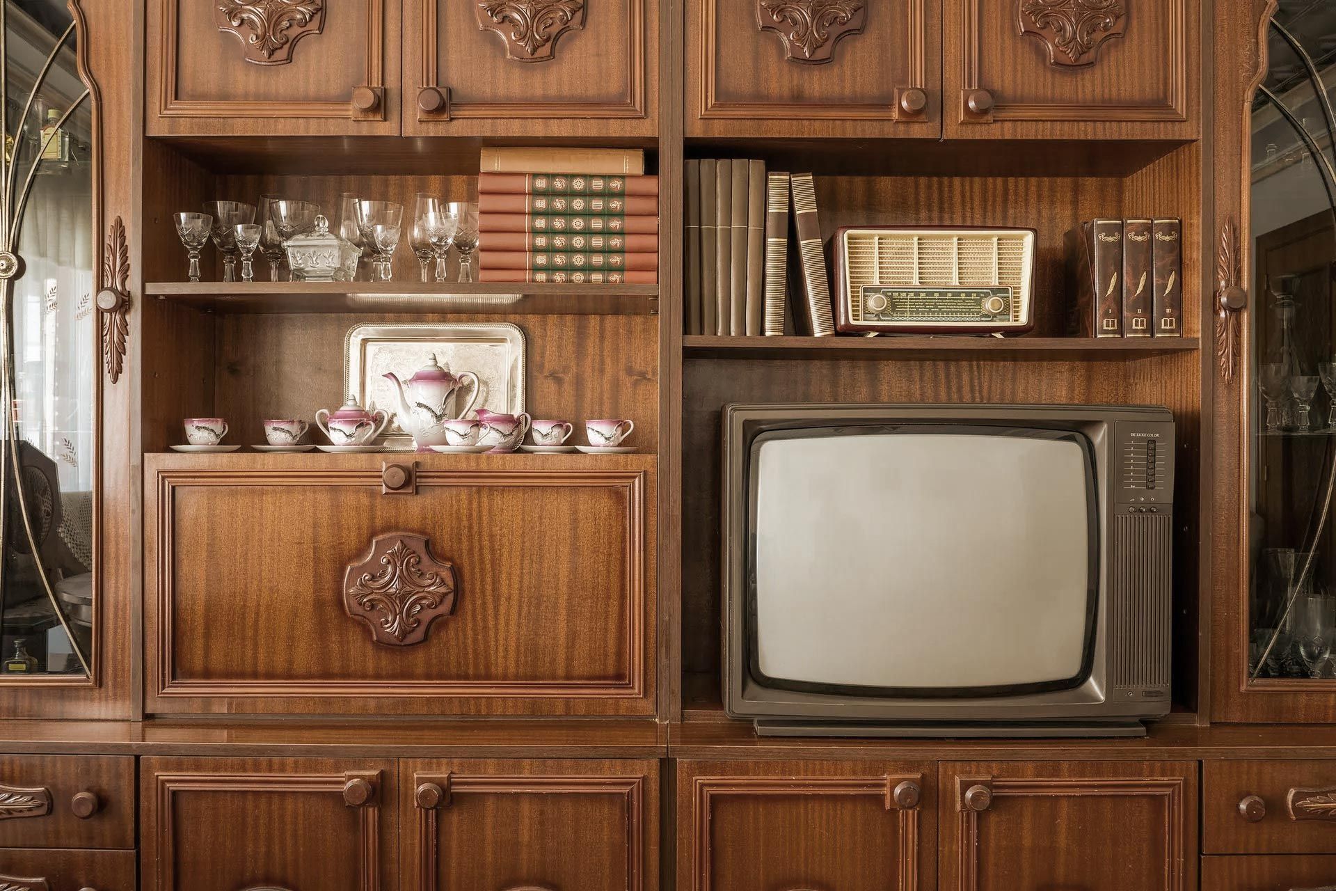 Wooden cabinet with vintage television, books, china, and glassware.