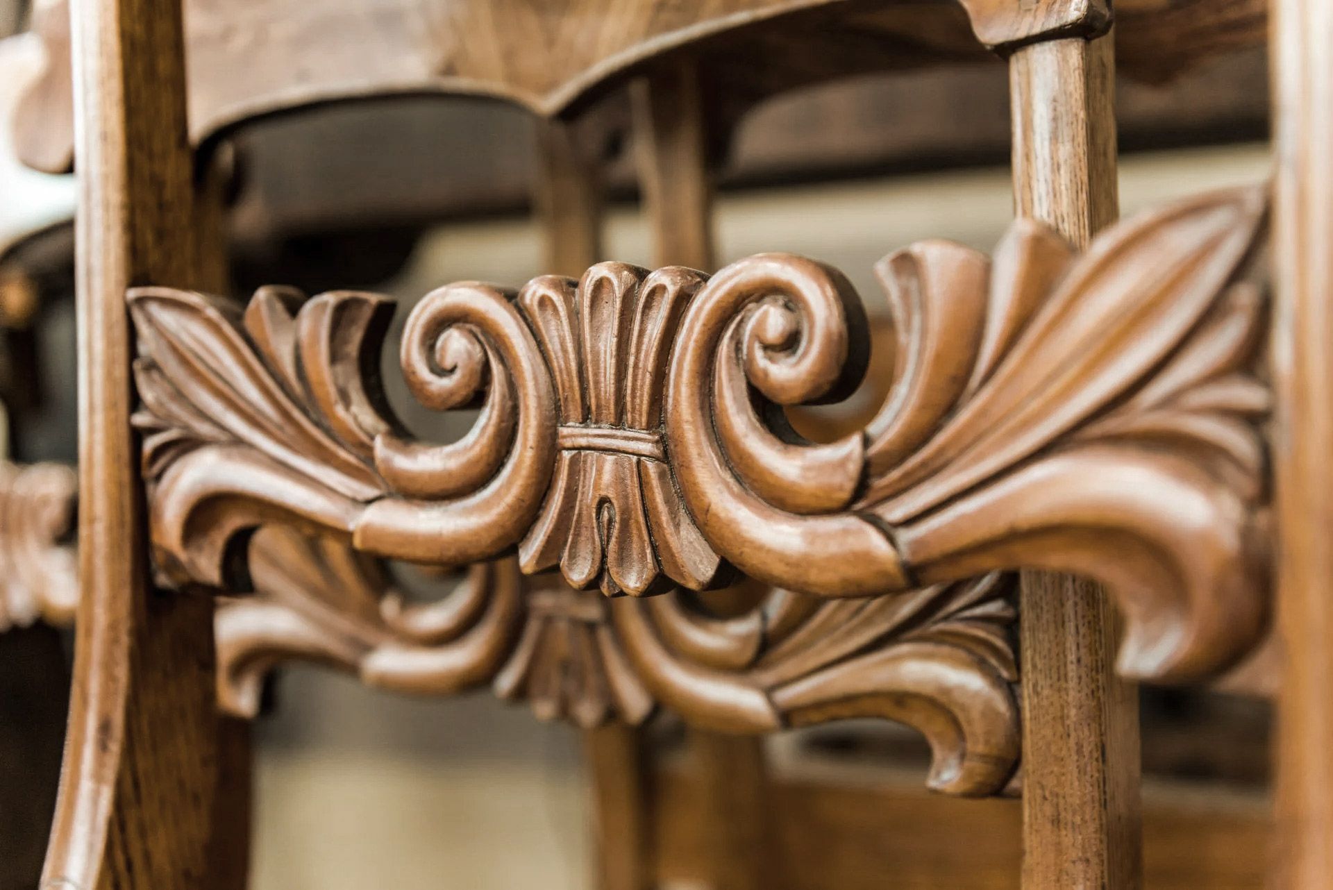 Ornate, carved wood detail on a chair, featuring scrolls and leaf shapes.