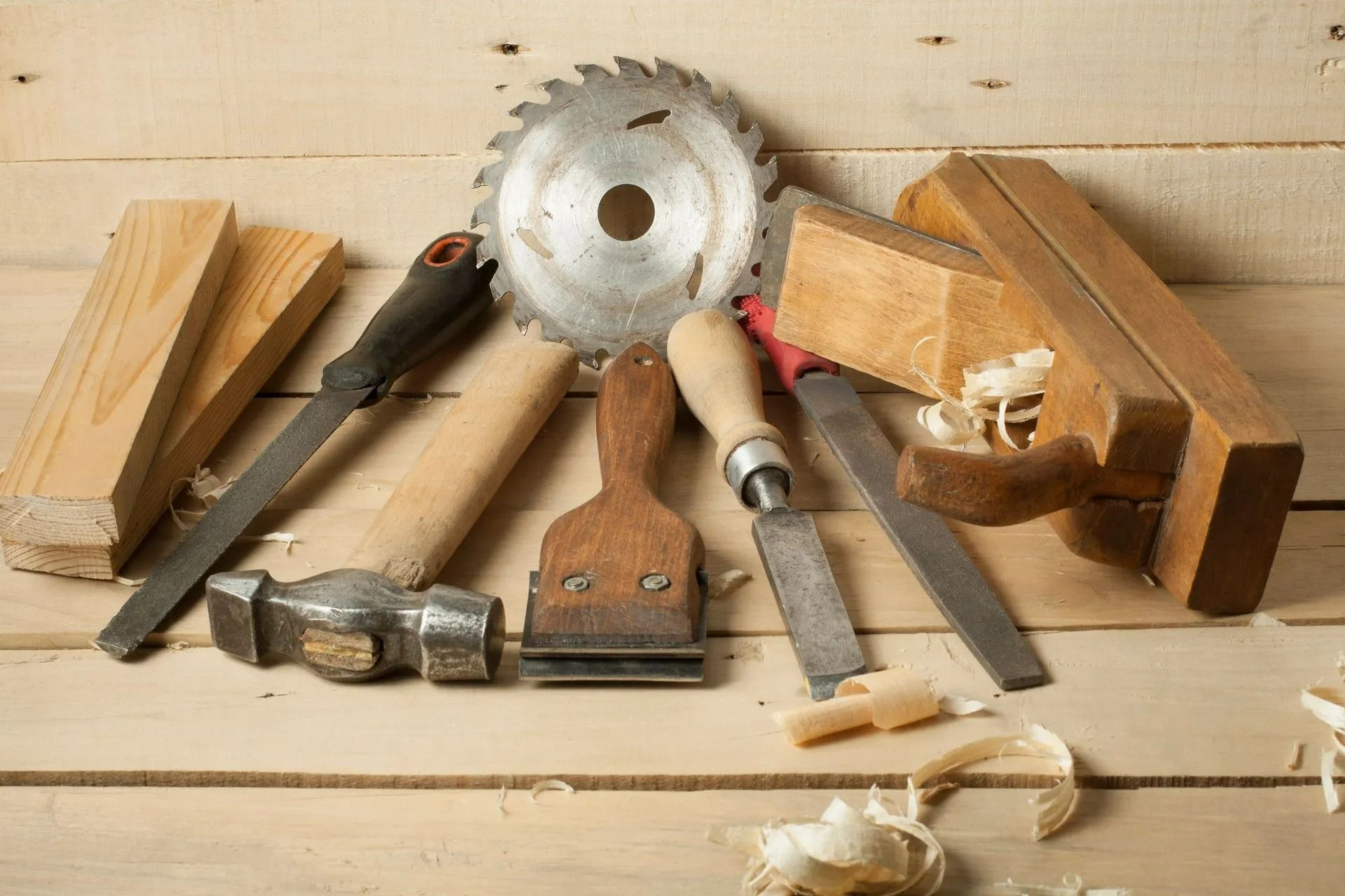 Carpentry tools on wooden planks: saw blade, plane, chisel, hammer, wood pieces, shavings.