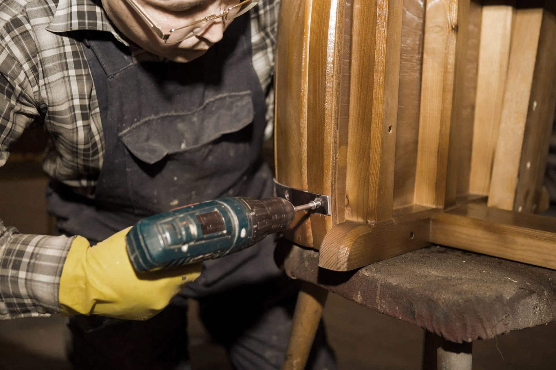 Person using a power drill on a wooden object, wearing gloves and safety glasses.