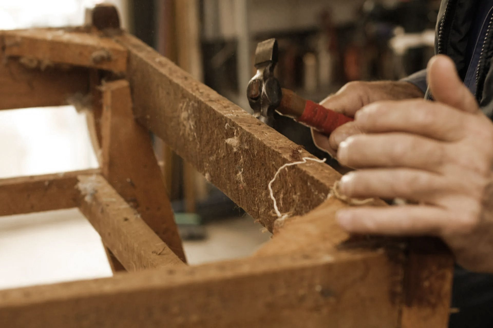 Person using a hammer to work on a wooden chair frame.