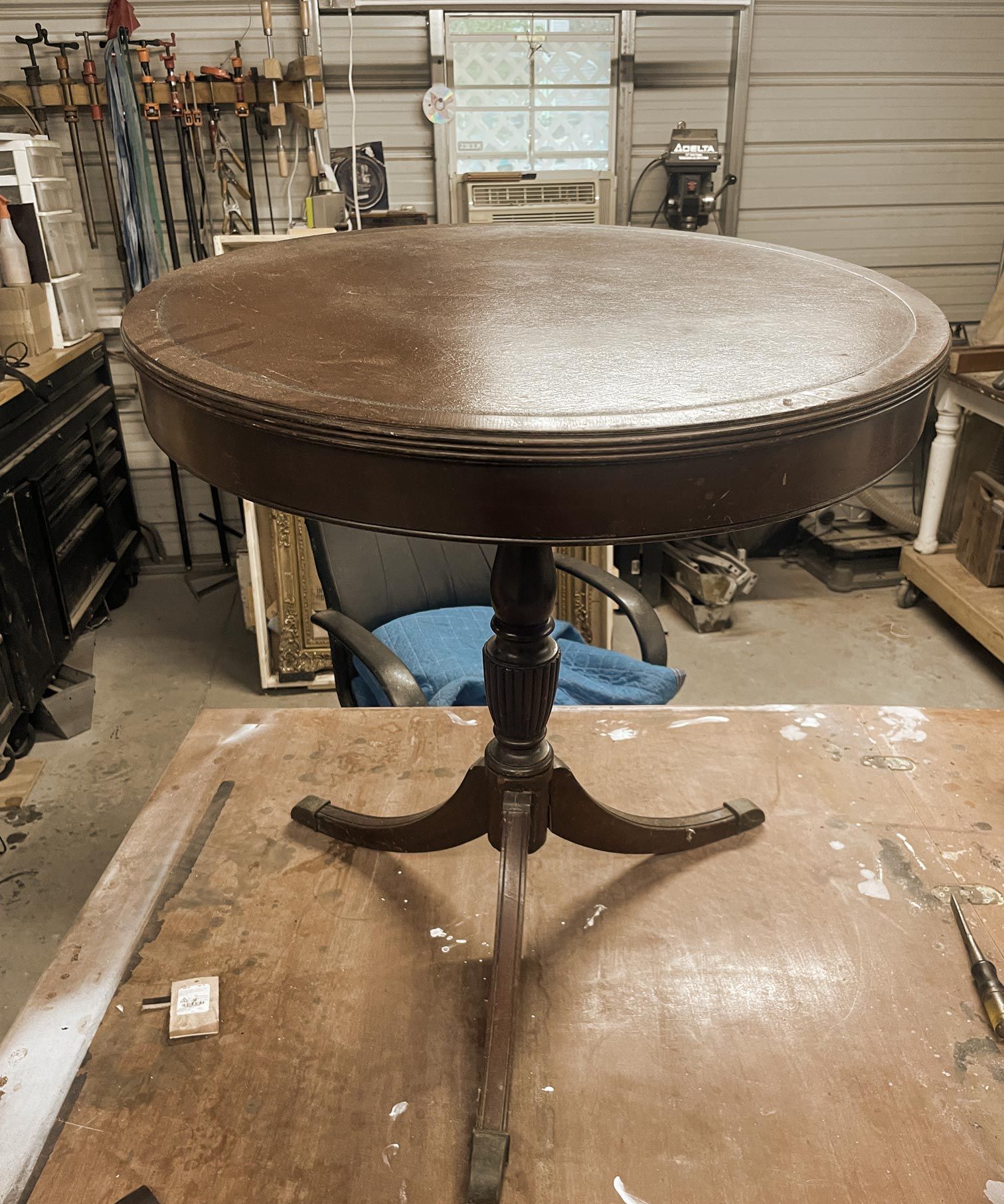 Antique wooden table with a leather top, half-cleaned, on a workbench in a workshop.