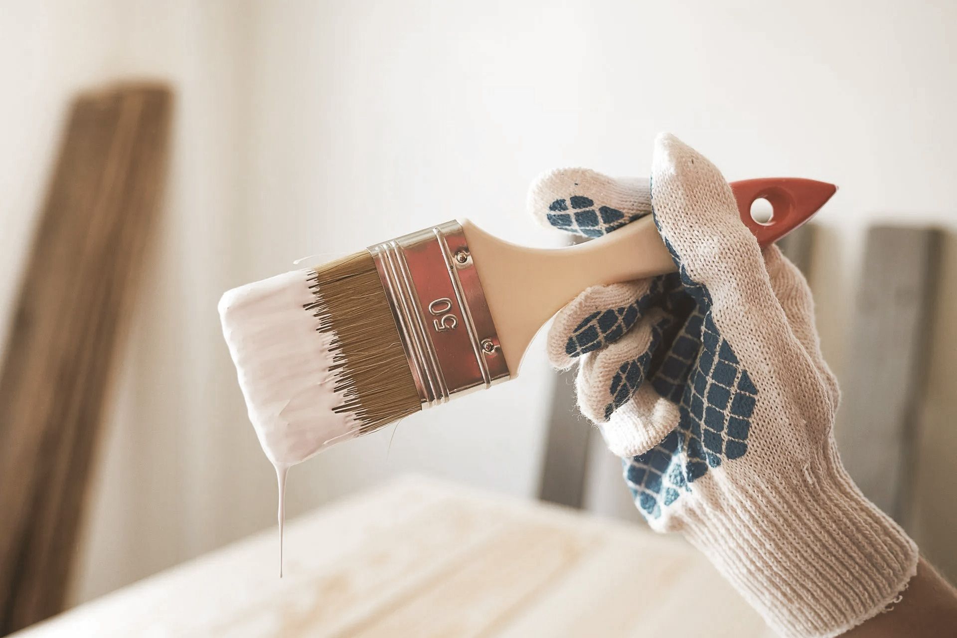 Hand in work glove holding a paint brush with dripping paint.