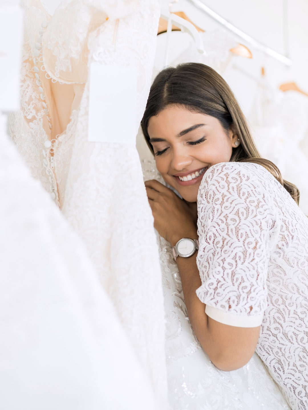 Woman smiles, hugging a wedding dress in a bridal shop.