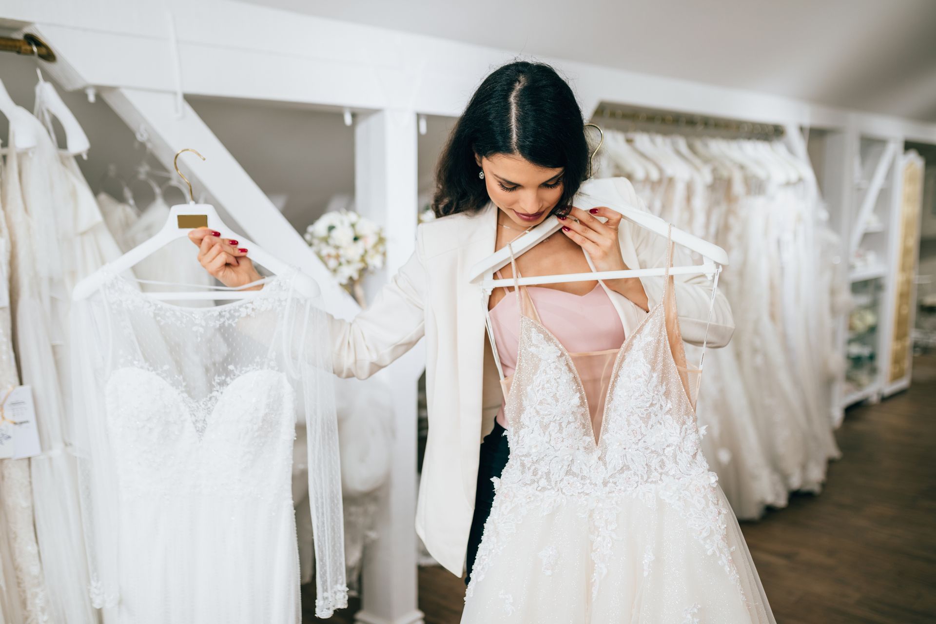 Woman examines two wedding dresses in a bridal shop, holding them up against herself.