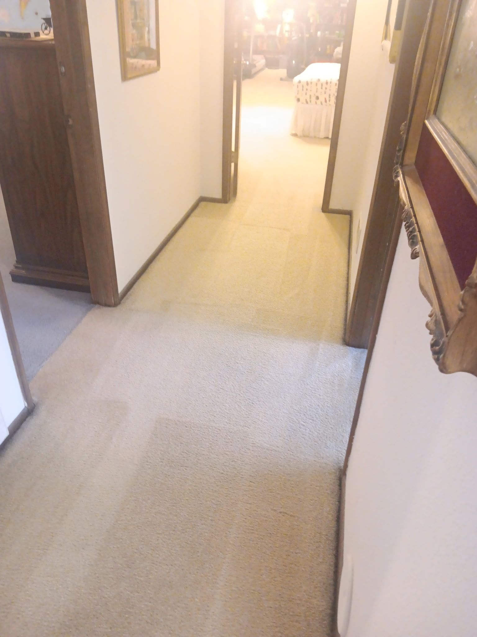 Person vacuuming carpet in living room. Yellow vacuum cleaner on the left, grey carpet, beige sofa, TV, cabinets, and teal curtains.