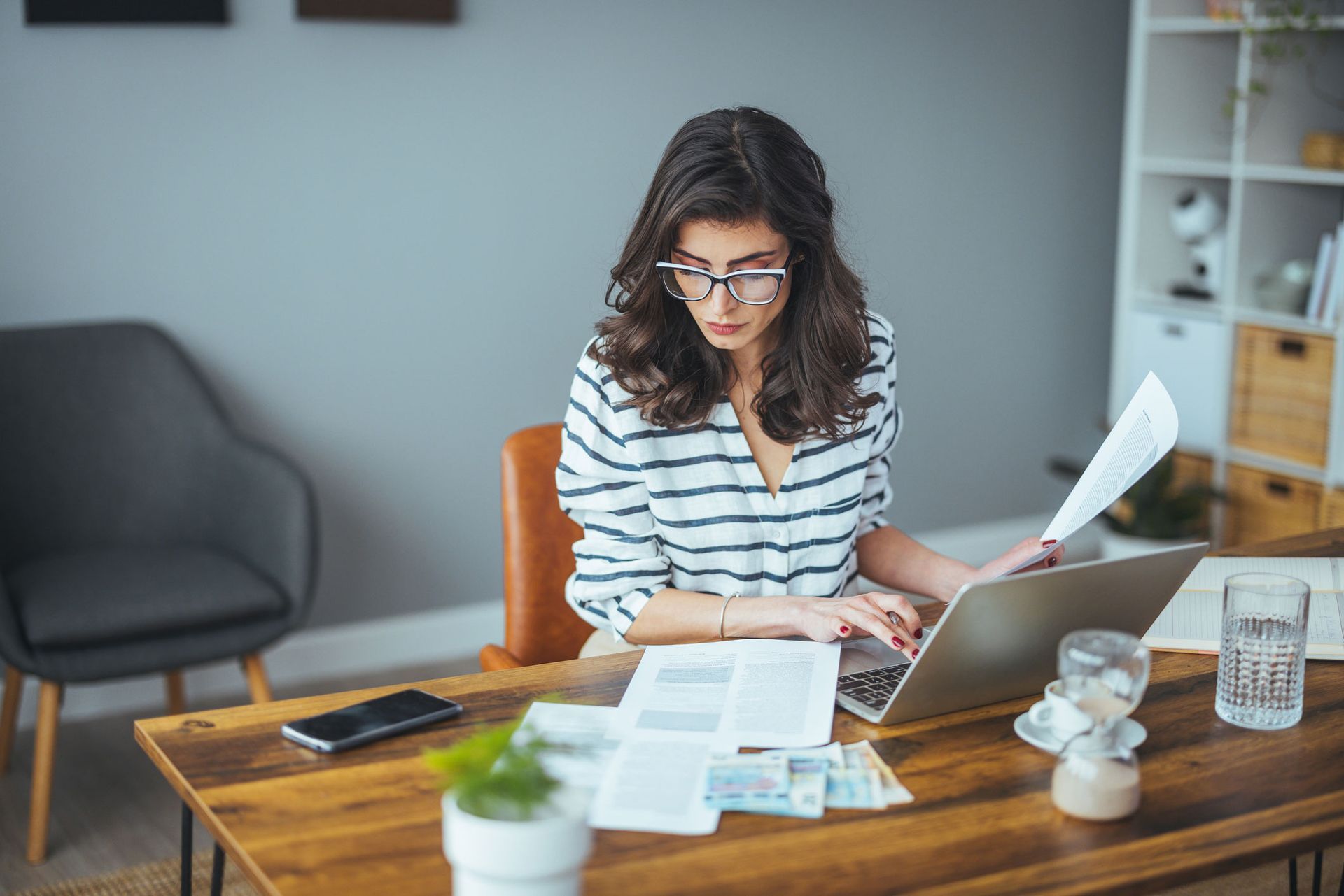 A woman is sitting at a desk with a laptop and papers.