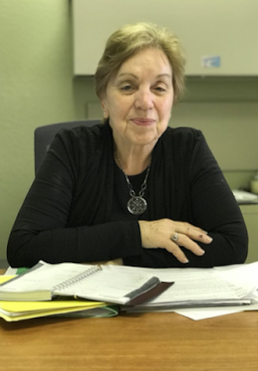 A Ruth in a black shirt is sitting at a desk with papers on it.