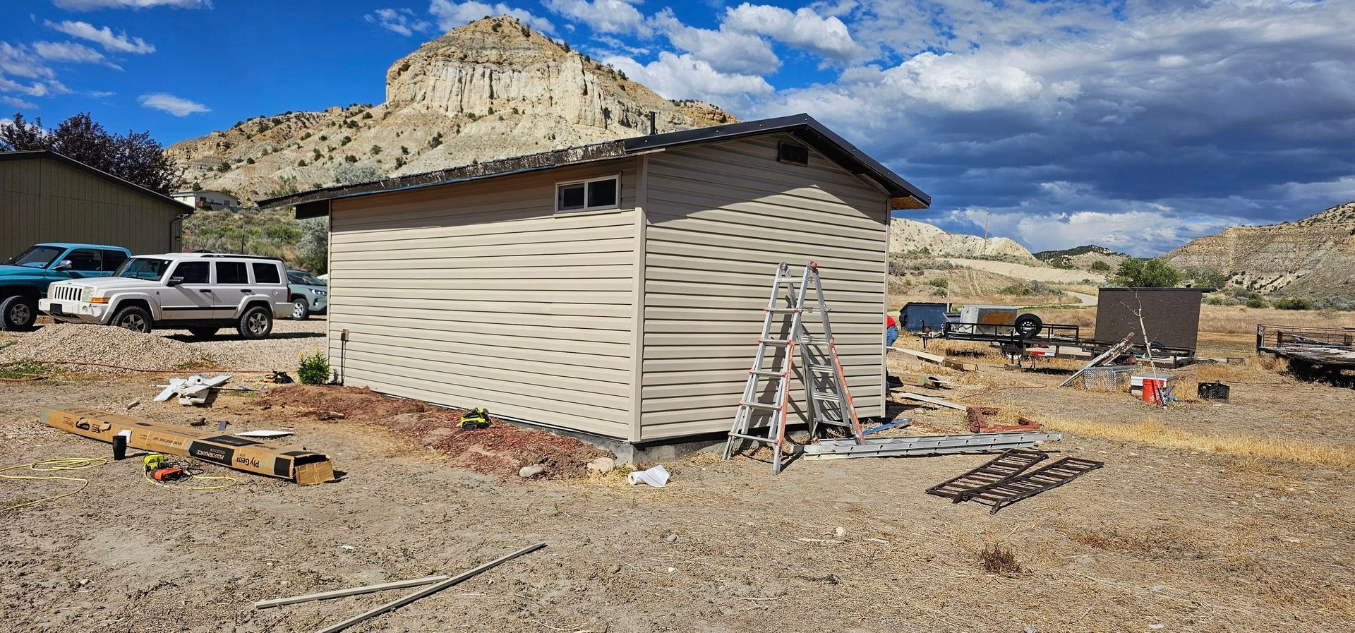 Building under construction with vehicles parked in front and a mountain in the background.