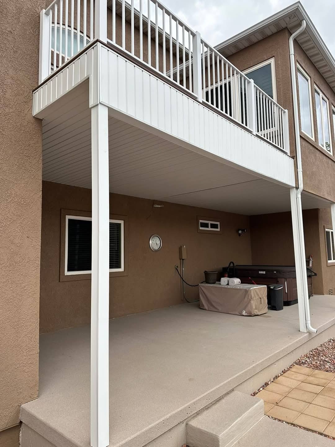 Two-story home with a deck; hot tub below. Tan stucco exterior, white railing, and supports.