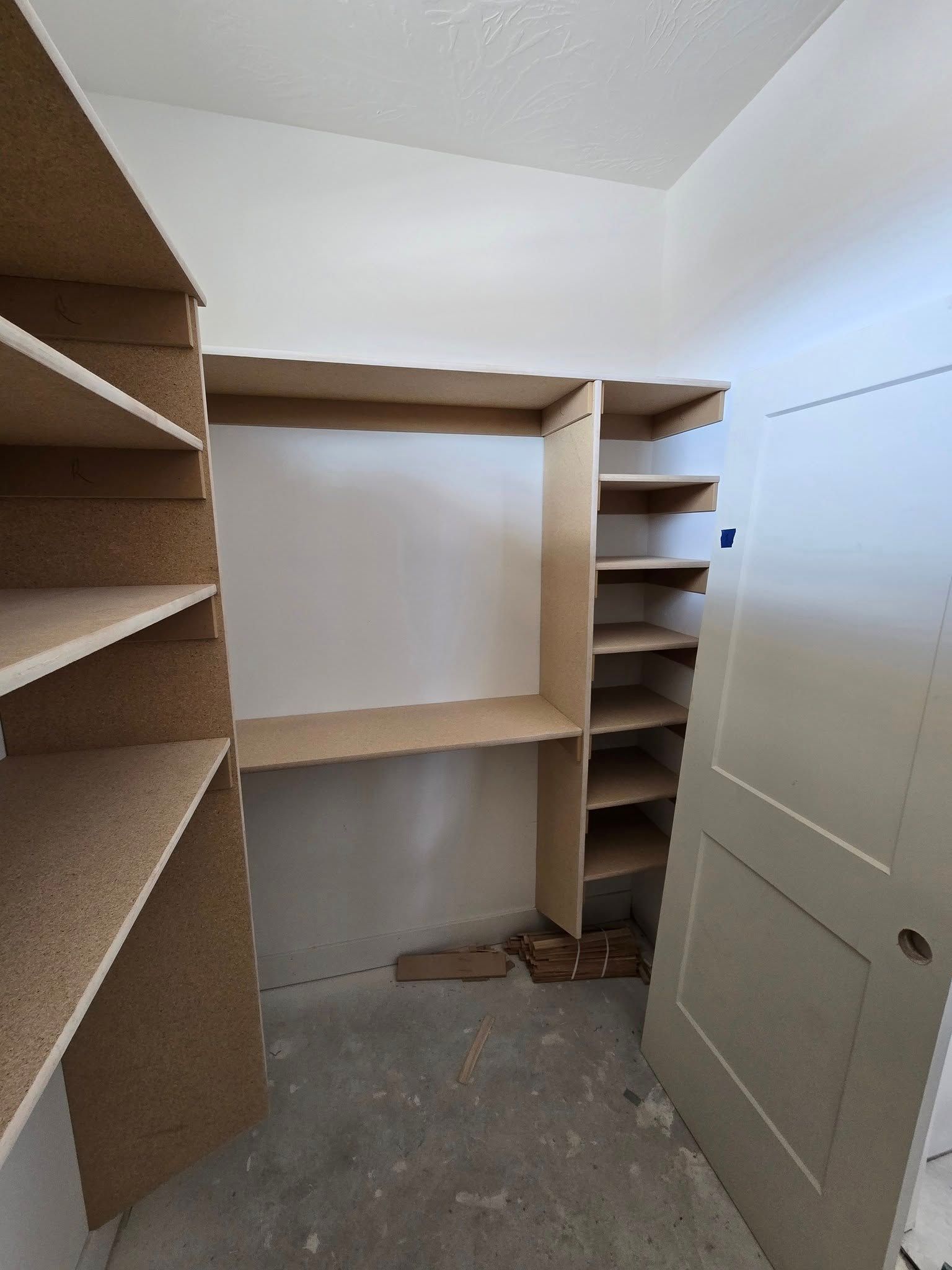 Empty closet interior with wooden shelves, door on right, unfinished concrete floor.