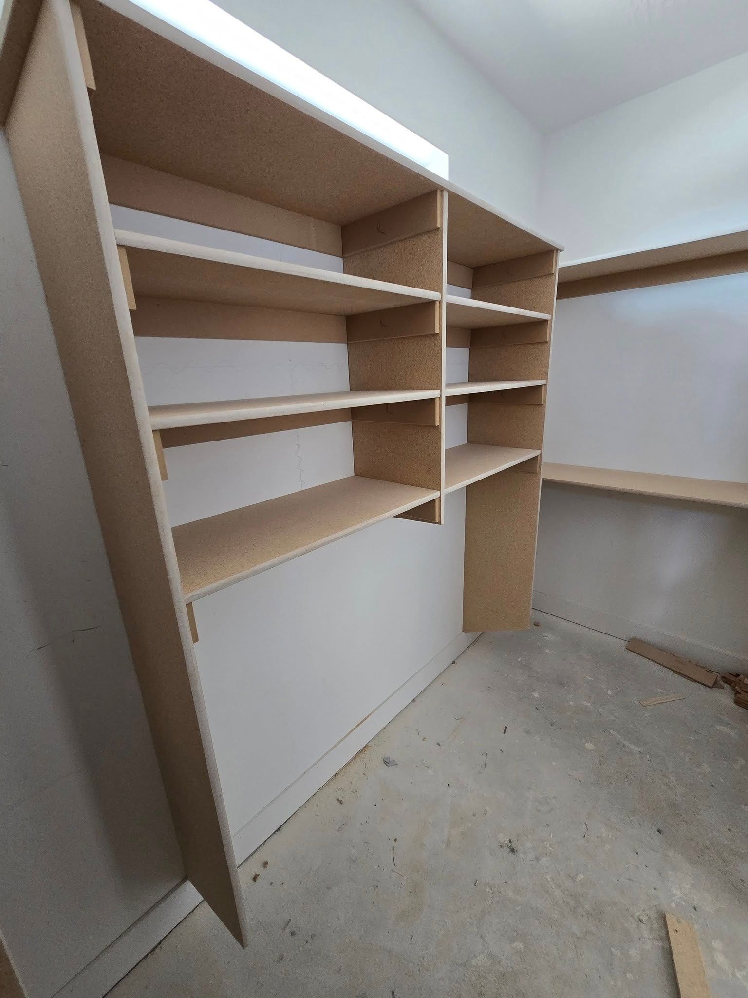 Built-in unfinished wood shelving unit in a room with concrete floor and white walls.