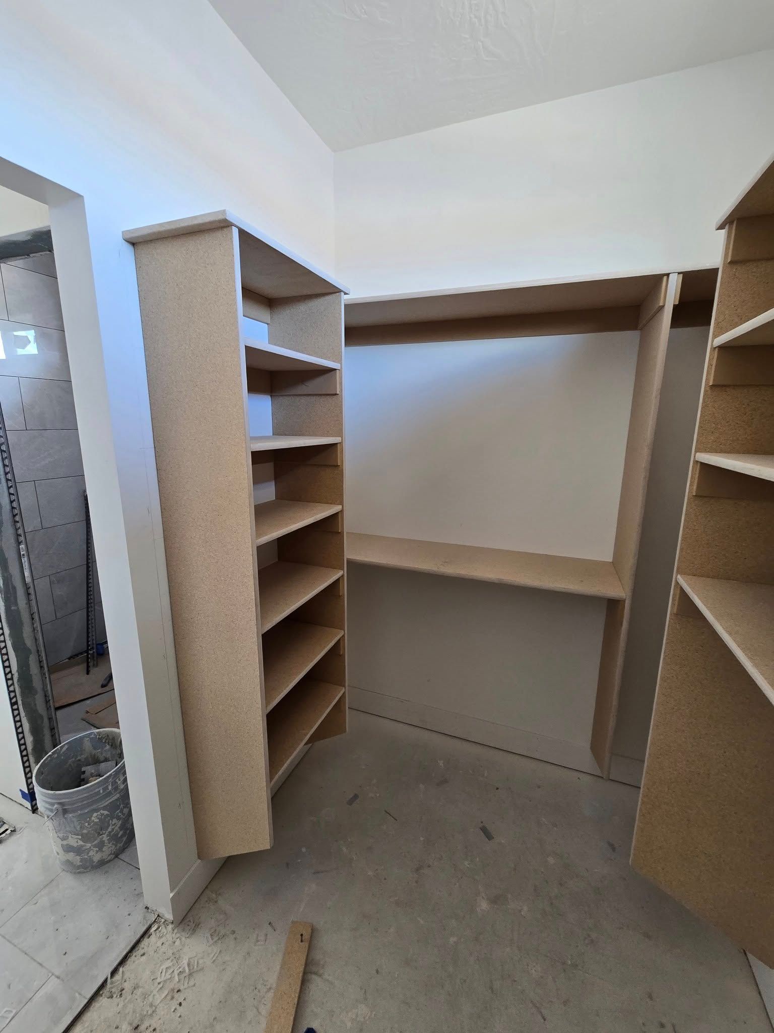 Closet shelving with unfinished particle board and shelves, in a room with concrete flooring.