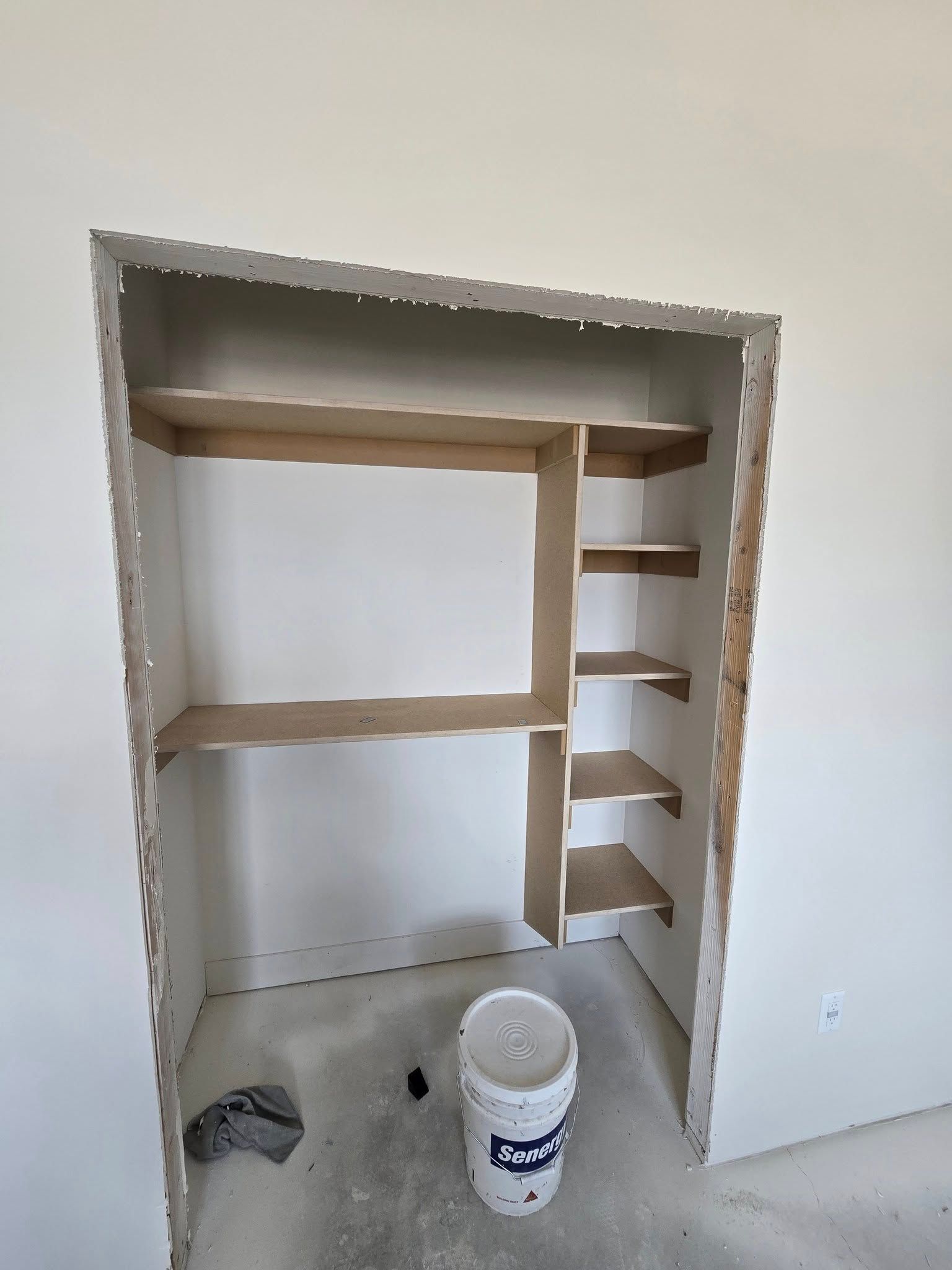 Empty closet with built-in shelving; unfinished walls and a bucket on the floor.