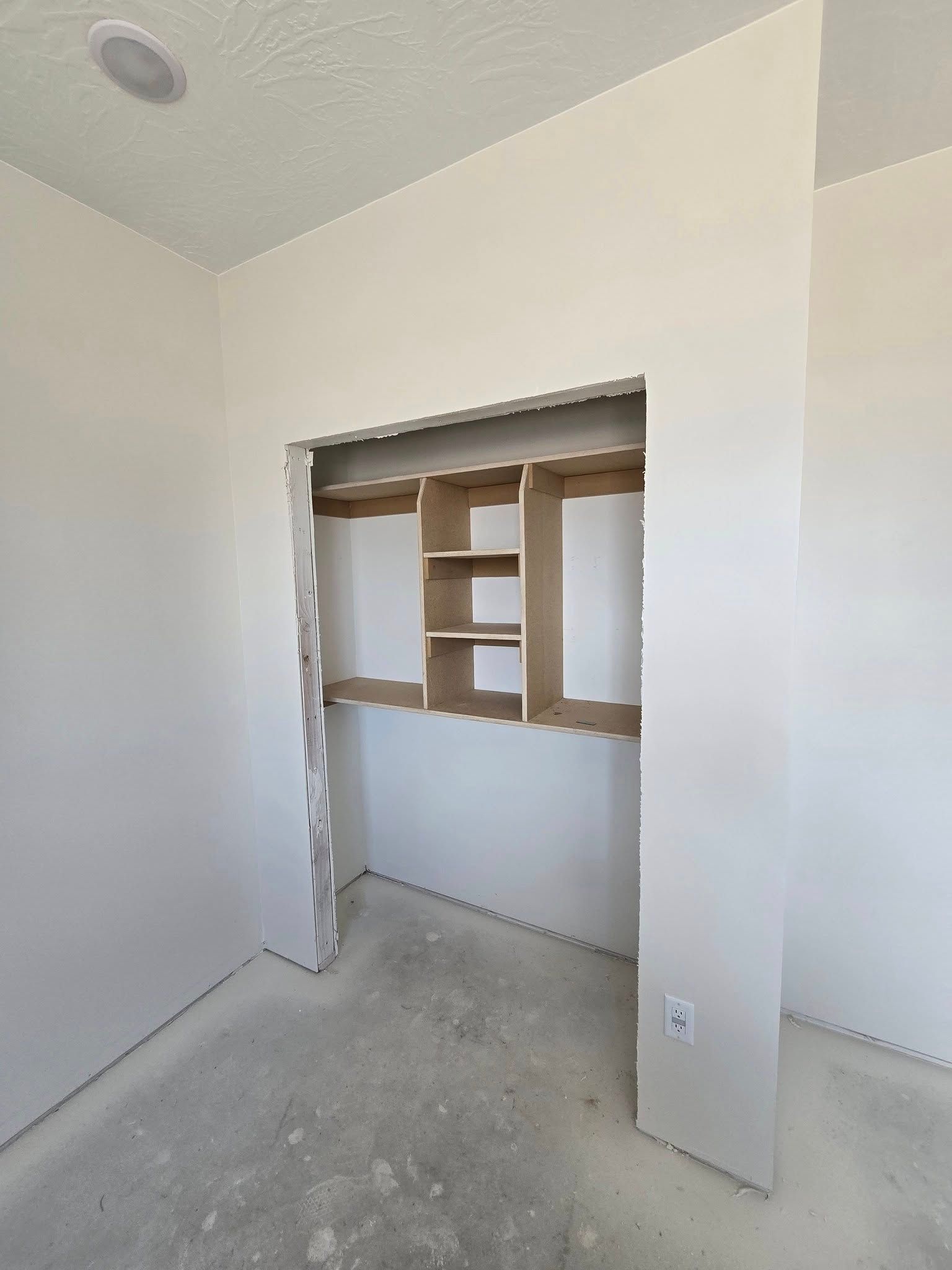 Empty walk-in closet, drywall walls, wooden shelves, and a light fixture in the ceiling.