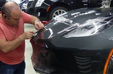 Un homme applique un film protecteur sur l'avant d'une voiture noire.