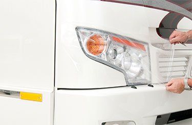 Une personne applique un film protecteur sur le devant d'un camping-car blanc.