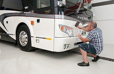 Un homme est agenouillé devant un camping-car blanc.