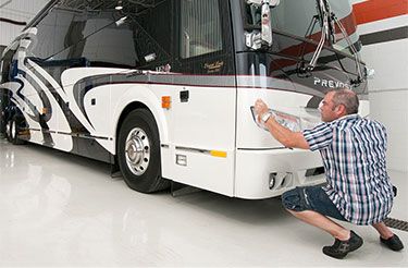 Un homme est agenouillé devant un camping-car blanc.