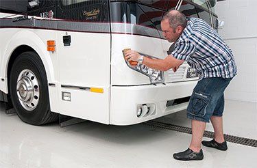 Un homme polit l'avant d'un bus blanc.