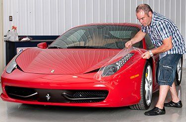 Un homme applique un film protecteur sur une voiture de sport rouge.