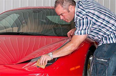 Un homme applique un film protecteur sur le capot d'une voiture de sport rouge.