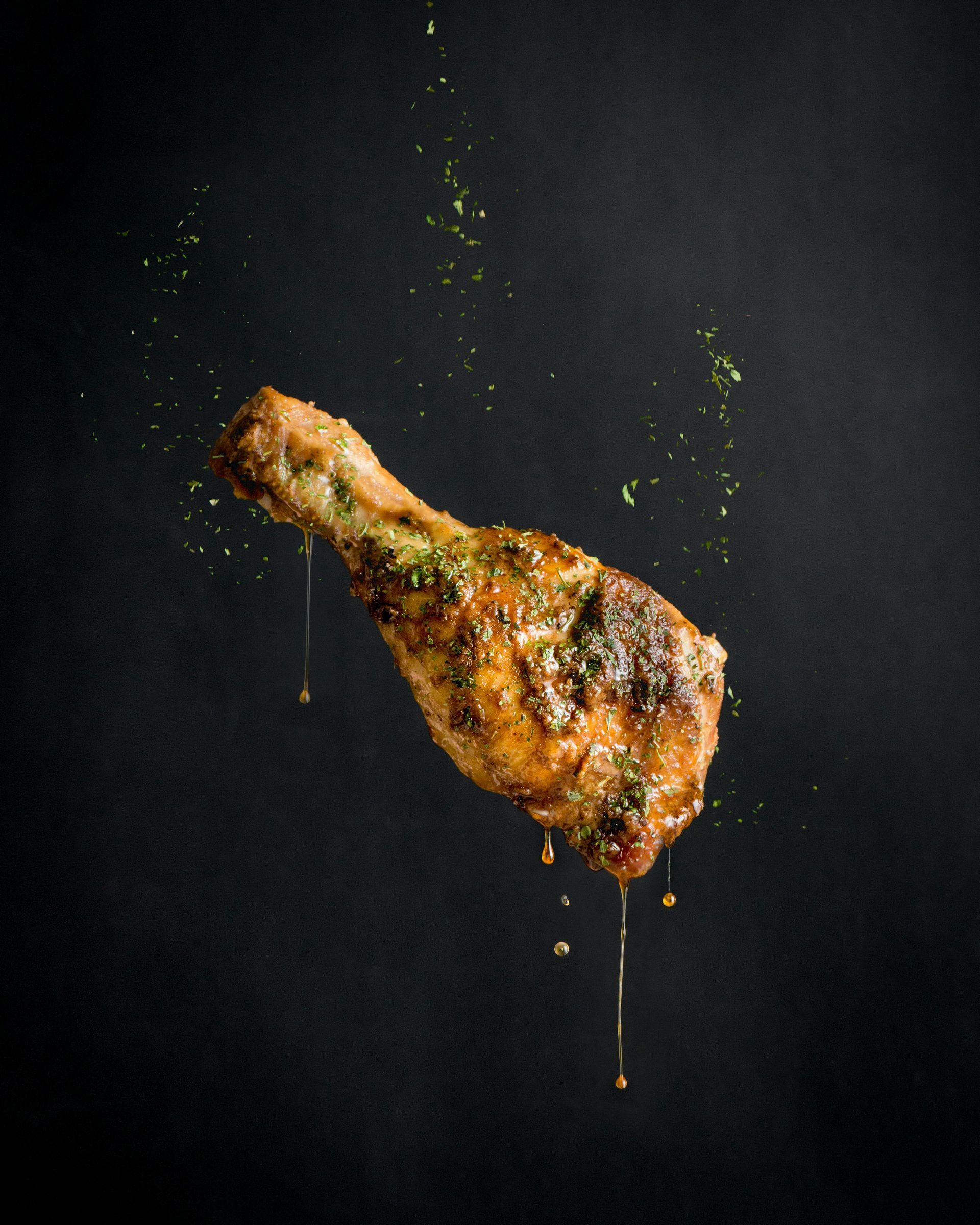 A chicken leg with sauce dripping off of it on a black background