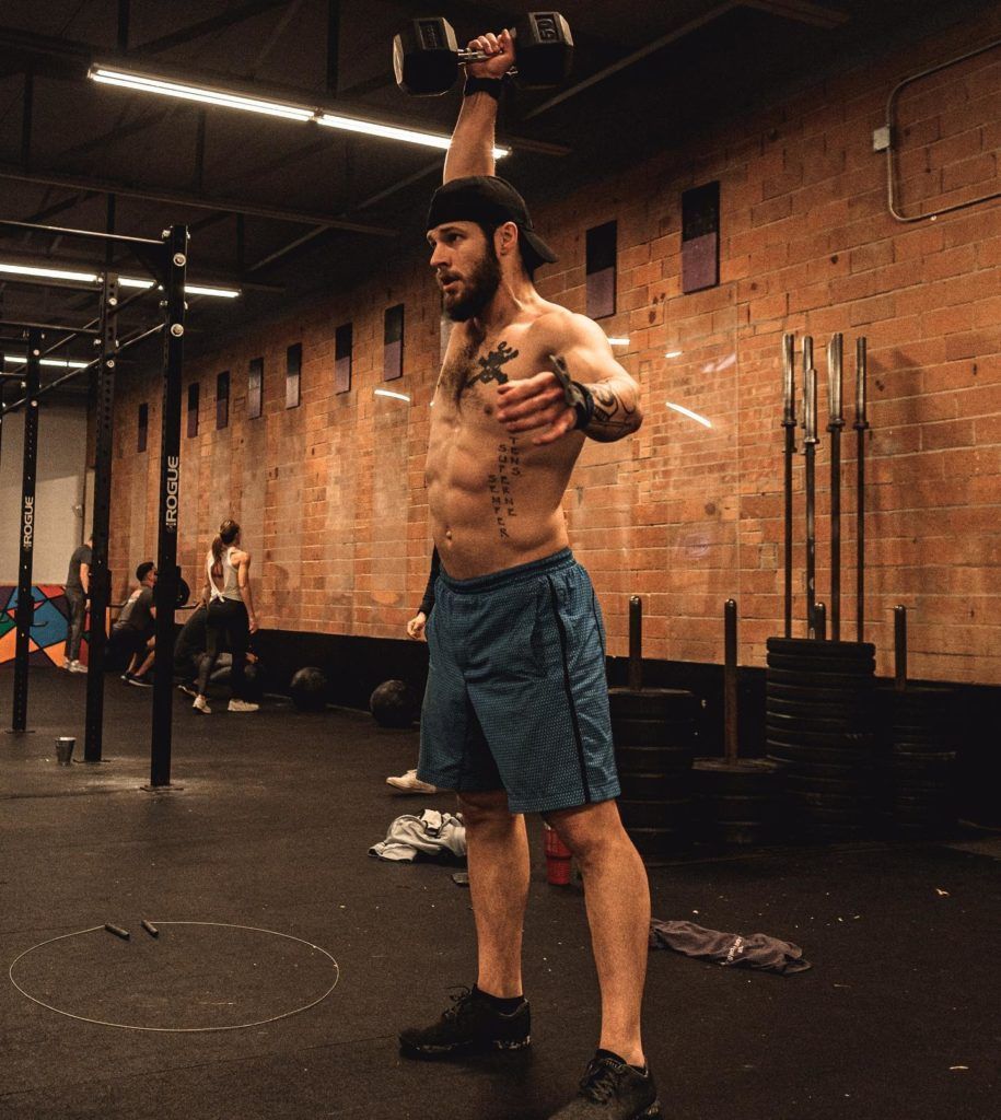 A shirtless man is lifting a dumbbell over his head in a gym.