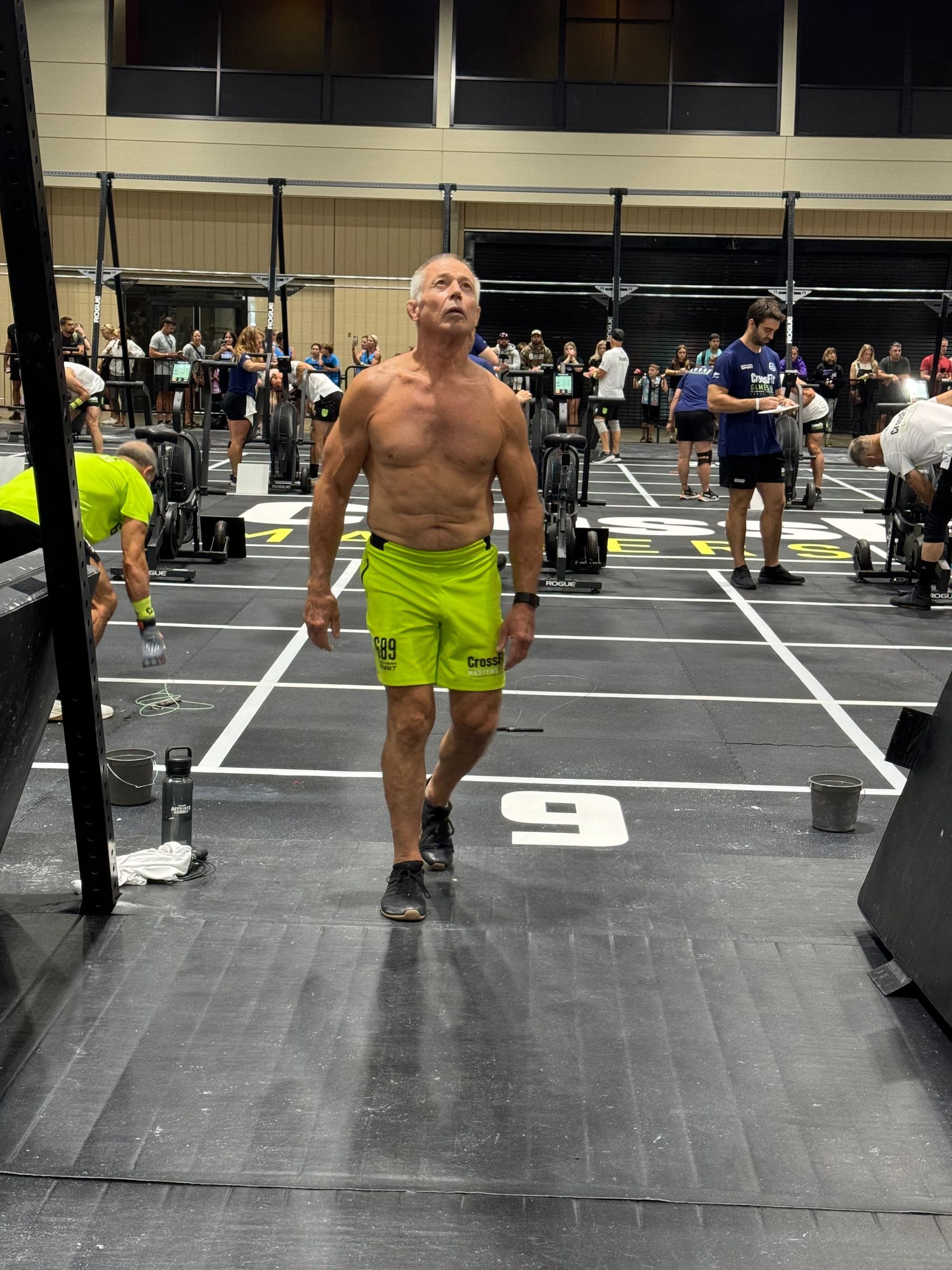 A shirtless man is walking in a gym with the number 9 on the floor