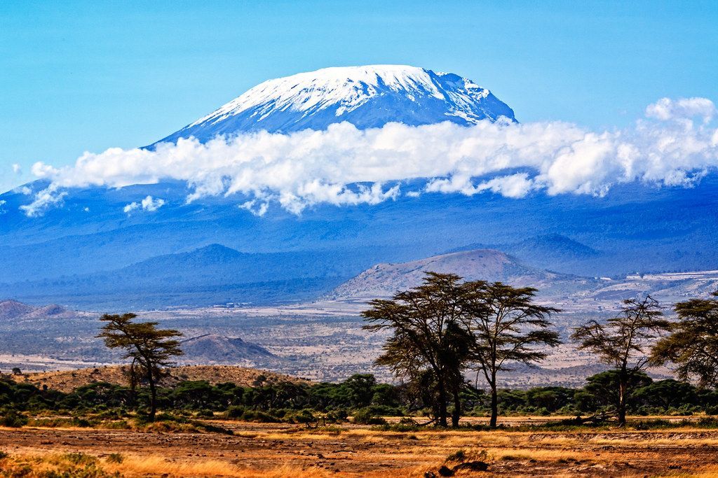 A mountain covered in snow is surrounded by trees and clouds in the distance.