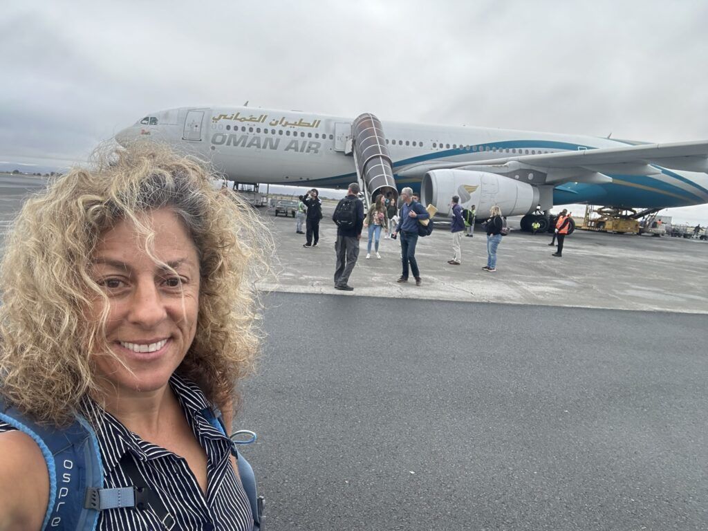 A woman is taking a selfie in front of an oman air plane.