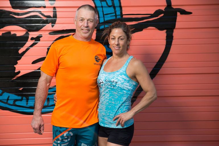 A man and a woman are posing for a picture in front of a pink wall.